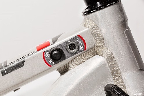 Close-up of an adaptive suspension control unit on a bicycle frame, featuring an on/off switch and charging port.